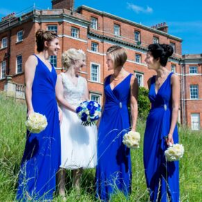 The bride chatting to her bridesmaids whilst standing in a summer meadow outside the main house