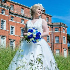 The bride outside the main house standing in tall grasses under perfect blue skies