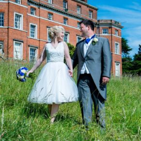 The newlyweds walking beside the main house through a grassy meadow