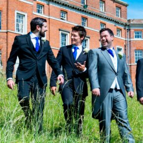 Photography of the groom and the lads taking a stroll through the tall grasses next to the main house at Brocket Hall on his wedding day at Brocket Hall