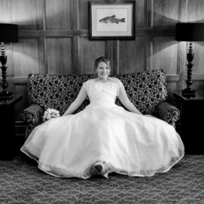 Photography of the bride taking a moment to relax on comfortable sofa in an oak panelled room at her wedding venue The Compleat Angler in Marlow