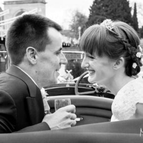 The newlyweds look at one another in their convertible vintage car