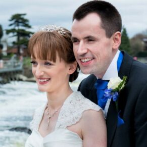 The newlyweds look across the river with the weir in the background beyond