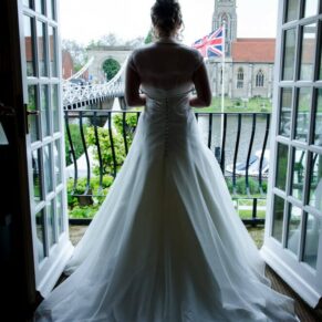 Silhouette photography of the bride framed in the doorway in the bridal suite at her Compleat Angler Hotel wedding with distant views over All Saints Church in Marlow