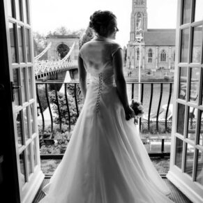 Photography of the bride framed in the doorway in the bridal suite at her Compleat Angler Hotel wedding with distant views over the River Thames and All Saints Church