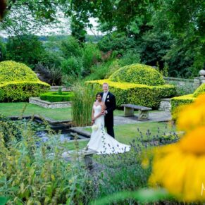 Danesfield House has so many hidden gems to explore in their fabulous gardens - an for us wedding photographers we are in absolute dreamland when we can use backdrops like the one you see here - for this capture I'm shooting through the flowers to add some depth and dreaminess to the final result - there's just so much for the eye to see in this striking image of the newlyweds The bride and groom captured through the summer flowers in the Italian Garden at their Danesfield House wedding