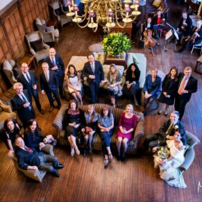 All of the wedding guests gathered in the Great Hall at Danesfield House look towards the balcony above for this group pose