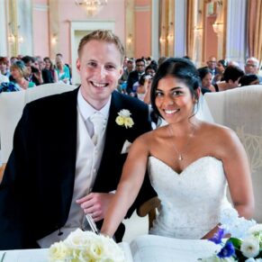 The smiling newlyweds signing the wedding register in the Versailles Suite at Danesfield House