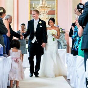 The smiling newlyweds exiting their wedding ceremony which took place in the Versailles Room at Danesfield House