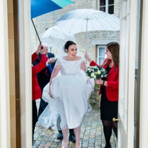 Fun candid capture of the bride arriving in the rain for her Hartwell House wedding