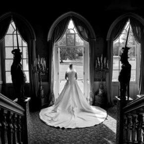 Dramatic high contrast black and white window shot of the bride captured through the Jacobean staircase looking towards the gardens at her Hartwell House wedding