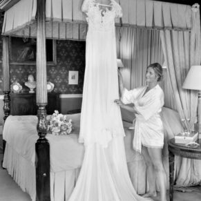 The bride adjusts her gown that's displayed on the four poster bed at her Hartwell House wedding