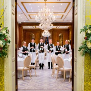 Hedsor House waiting staff posing for a picture captured through the doorway and into the dining room at a wedding