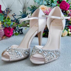 The bride's glimmering shoes placed onto a pale grey chair with her vibrant bouquet