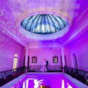 Classic and dramatic pose of the newlyweds on the balcony in the Great Hall lit with Hedsor House's bright and vibrant disco lighting
