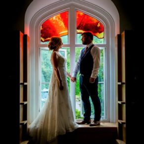 Striking silhouette shot of the newlyweds captured in one of the venue's majestic floor to ceiling stained glass windows