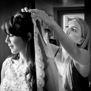 The bride pre ceremony with her bridesmaid making adjustments to the veil captured with dramatic window lighting