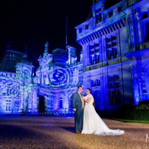 Dramatic floodlit pose of the bride and groom in front of Waddesdon Manor after dark