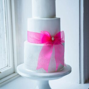 The white cake adorned with a pink ribbon for the bride and groom at their Grove Hotel wedding