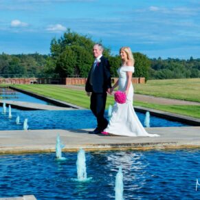 The couple take a walk near to the lovely water feature in The Grove Hotel's grounds on their summery wedding day