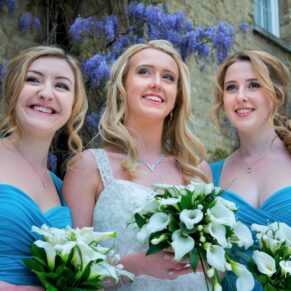 Photography of the smiling bride and her bridesmaids looking away from the camera as they stand in front of the flowering wisteria at this stunning Beaumont Estate wedding