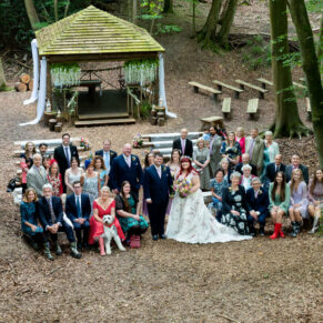 Large group pose of all the guests captured in the woodland dell soon after the marriage ceremony