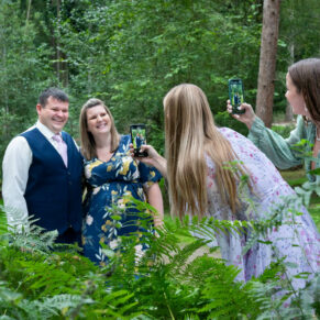 Candid woodland moment of guests taking photos through the woodland ferns at this woodland gathering