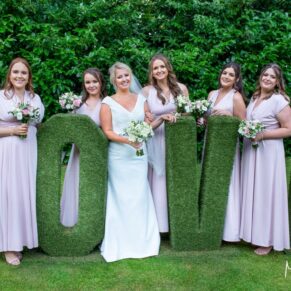 The ladies pose beside the giant topiary love letters, captured at The Grange, Northwood wedding