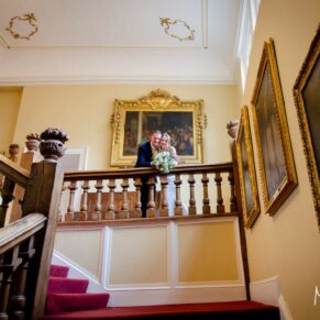 The newlyweds on the grand staircase on their wedding day at Farnham Castle