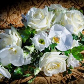 Beautiful bride's bouquet of white roses and orchids placed elegantly on an opulent gold fabric and illuminated with dramatic window lighting at Hedsor House