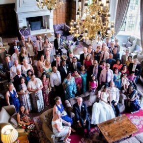 A large group pose of all the wedding guests captured from above in the dramatic high ceilinged Great Hall at Danesfield House Hotel