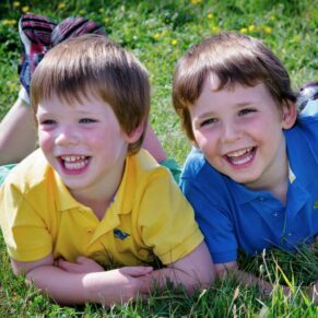 Two brothers in vibrant colours giggling for the camera whilst laying down in the tall grasses
