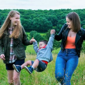 Two sisters swing their brother into the air during their Buckinghamshire family portraits session - pictures can be as candid as you like for your photography session