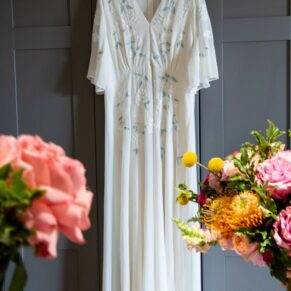 The bride's wedding gown hanging up on a doorway surrounded by colourful flowers at The Crazy Bear Hotel in Stadhampton