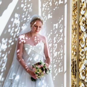 Bride poses beside the Golden Gates with dappled light illuminating the pose to dramatic effect at her Cliveden House wedding