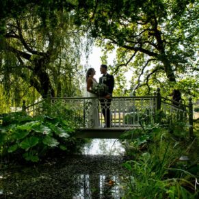 Atmospheric silhouette pose of the newlyweds on the bridge with their reflection seen in the water below