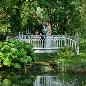 The bride and groom on the bridge surrounded by lush green summer foliage in this romantic garden setting