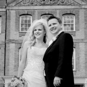 The smiling newlyweds pose for the camera with the stunning venue behind in the distance