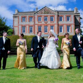 The smiling bridal party walk towards the camera under near perfect blue skies with the main house behind in the distance