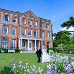 The bride and groom take a stroll in the gardens in front of the main house with wonderful vibrant flower borders in the foreground