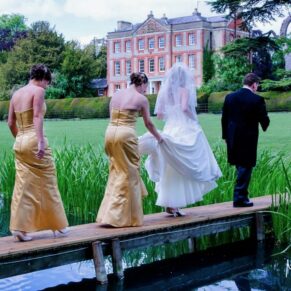 The bride is carefully helped across the narrow wooden bridge after her marriage ceremony