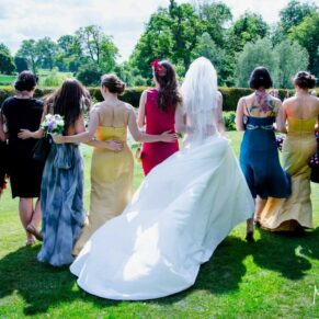 The ladies in brightly coloured dresses walk away from the camera in the gardens at this Oxfordshire summer wedding