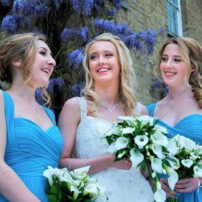The bride chatting with her bridesmaids in front of the flowering wisteria during the drinks reception at her summer wedding