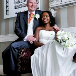 The newlyweds in a relaxed photography pose sit on a chair by the window at the top of the grand staircase during their Beaumont Estate wedding