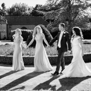 Black and white photography of the bride and groom walking with their bridesmaids at their historic Buckinghamshire wedding venue Hampden House