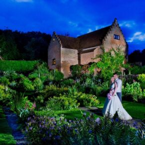 Stunning and surreal floodlit pose of the newlyweds captured after night fall on their wedding day with colourful flowers all around at their Hertfordshire venue Chenies Manor