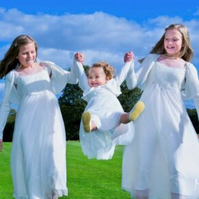 A fun shot of the bridesmaids swinging the flower girl into the air at this relaxed summer drinks reception