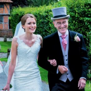 The very relaxed bride and her father approach the church through the village centre on the quiet roads
