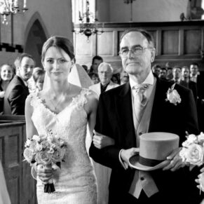 The bride enters the parish church on her fathers arm with her family and friends watching on from the pews