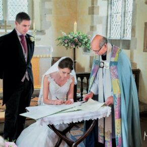 The newlyweds signing the register in the parish church under the watchful eye of the vicar